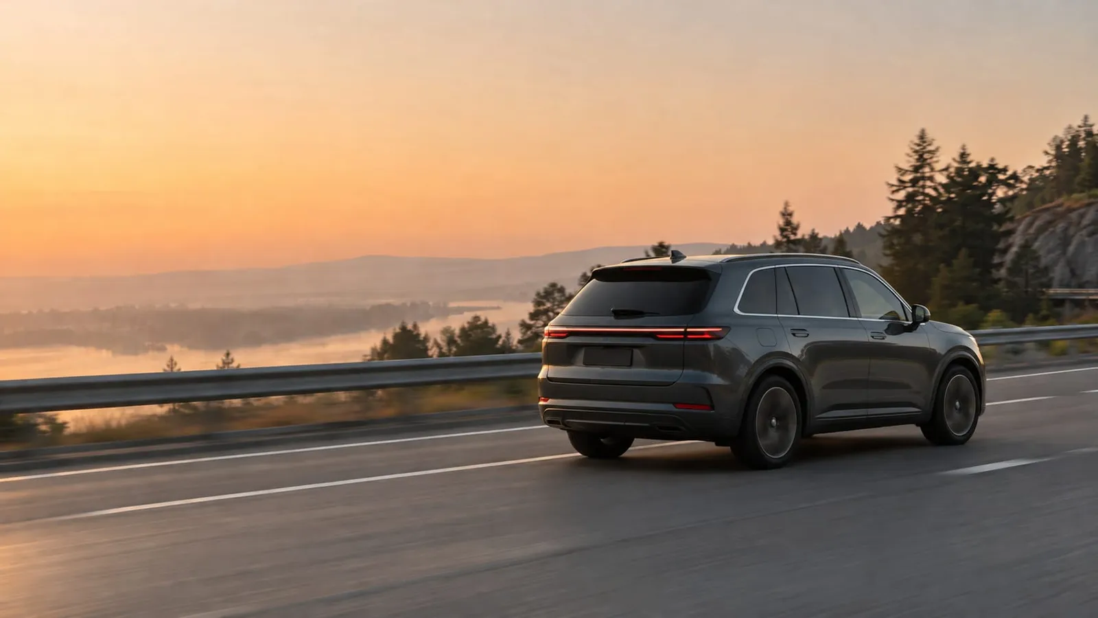 A dark gray SUV seen from behind driving on a highway above a lake at sunrise