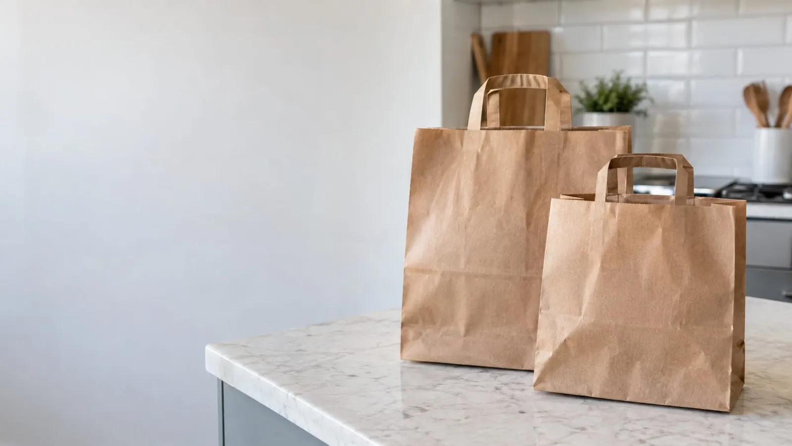 Two kraft paper bags with handles standing on a marble kitchen counter